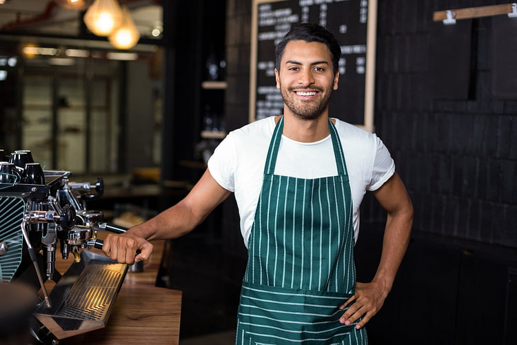 Smiling barista standing next coffee machine in the bar